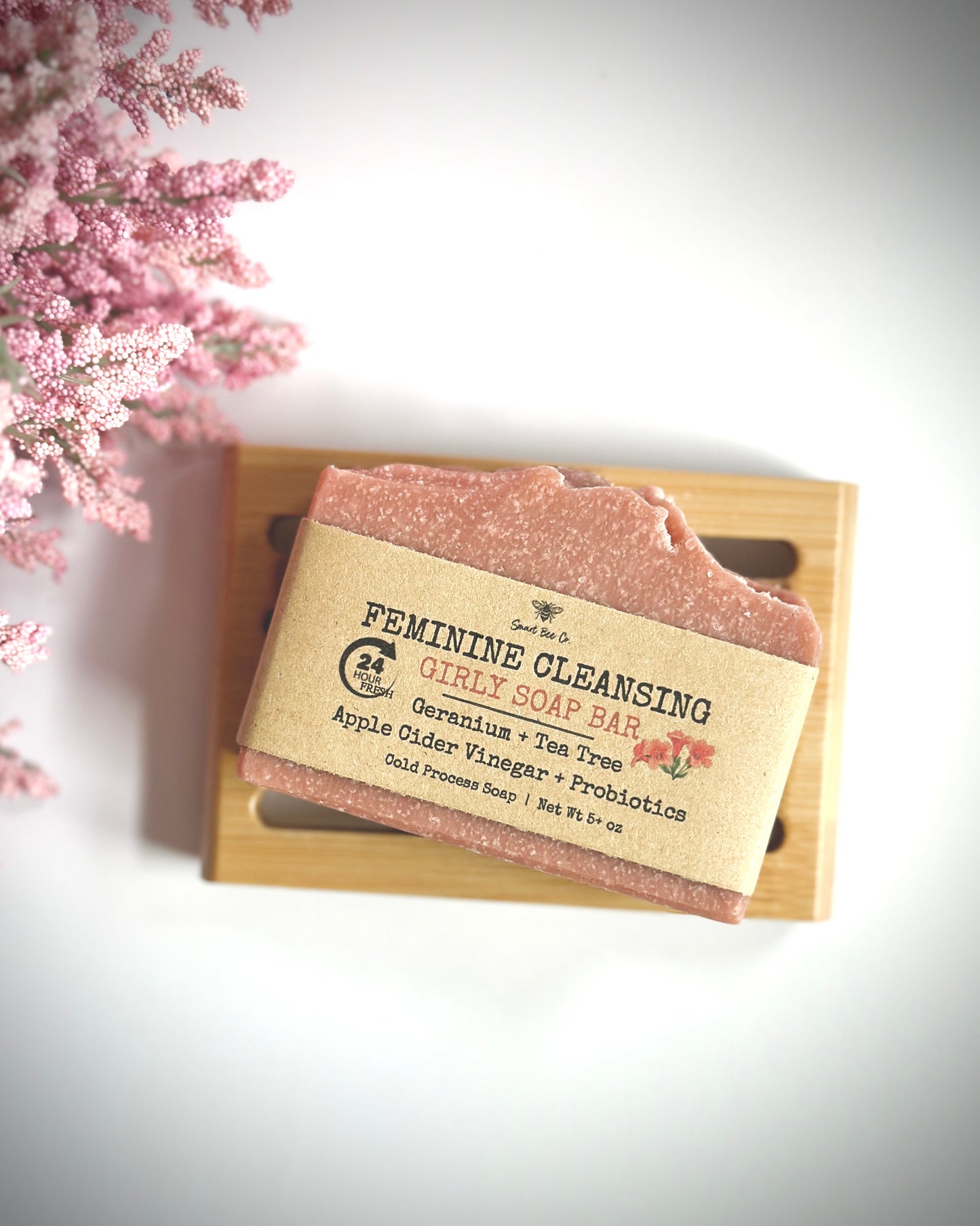 Feminine cleansing soap bar on a wooden tray with pink flowers in the background
