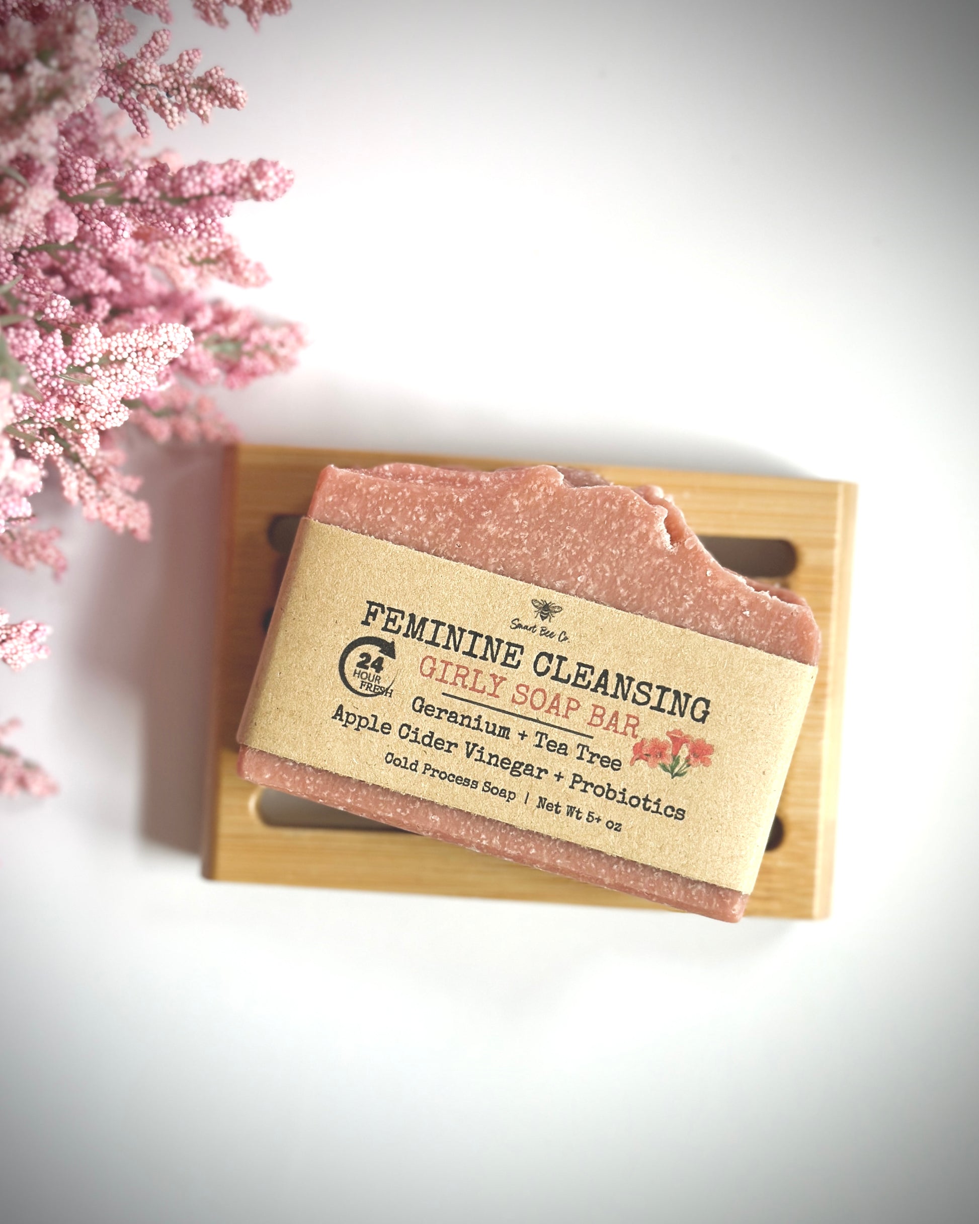 Feminine cleansing soap bar on a wooden tray with pink flowers in the background