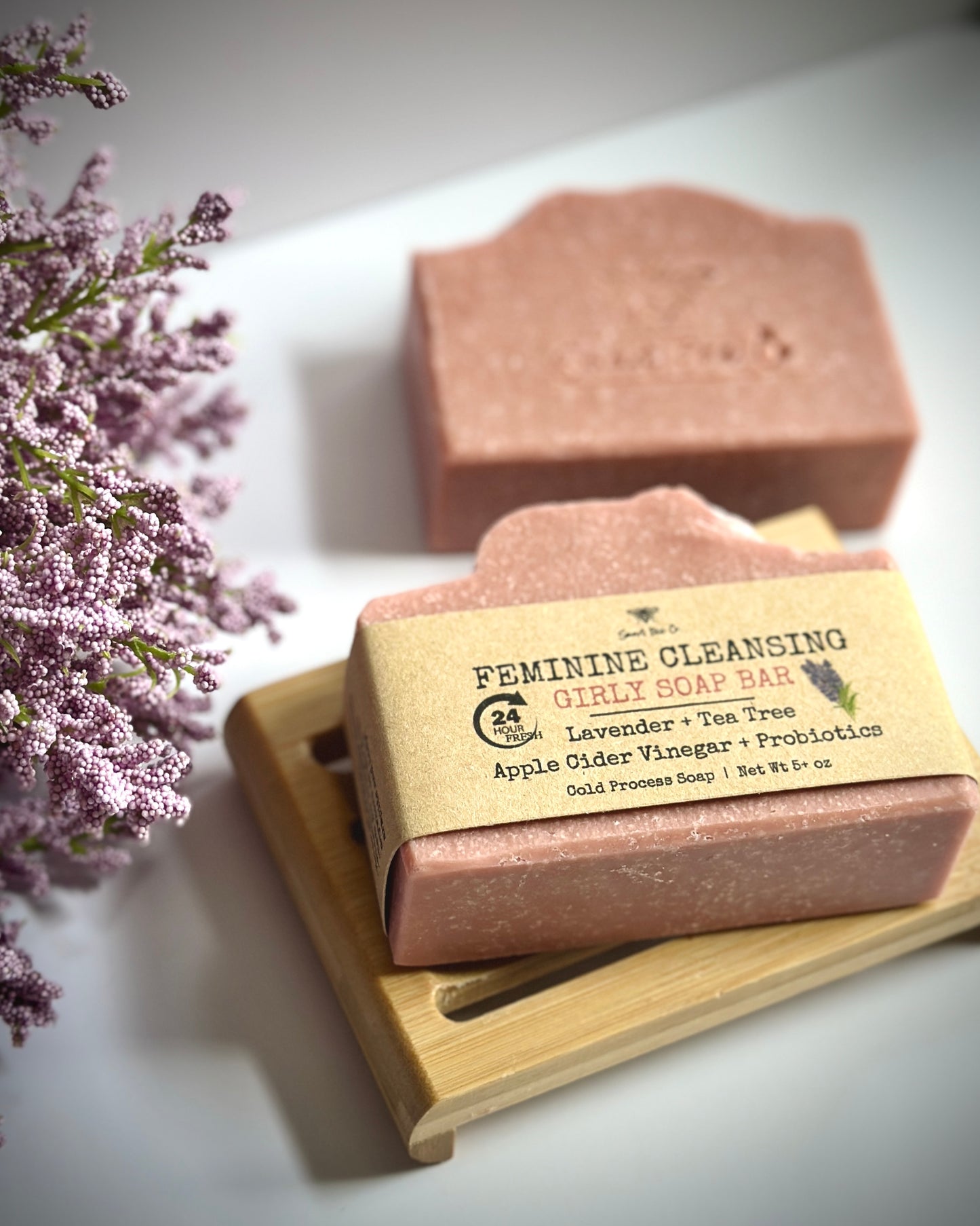 Two soap bars on a wooden stand with a label, surrounded by purple flowers.