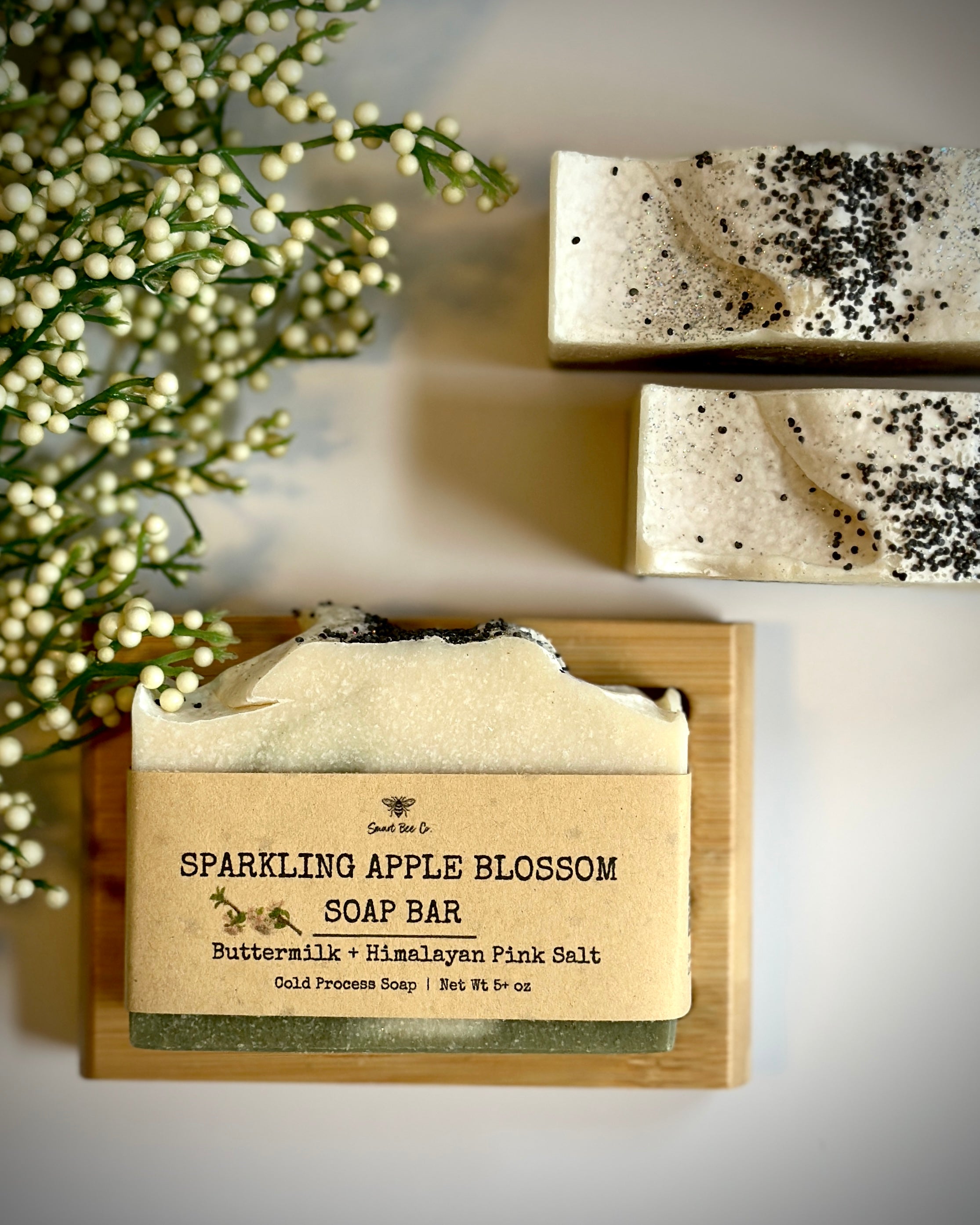 Sparkling Apple Blossom soap bar with a label on a wooden block, surrounded by greenery.