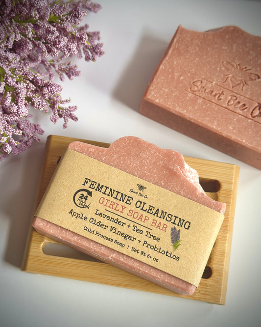 Feminine cleansing soap bar with packaging on a wooden board, surrounded by lavender flowers.