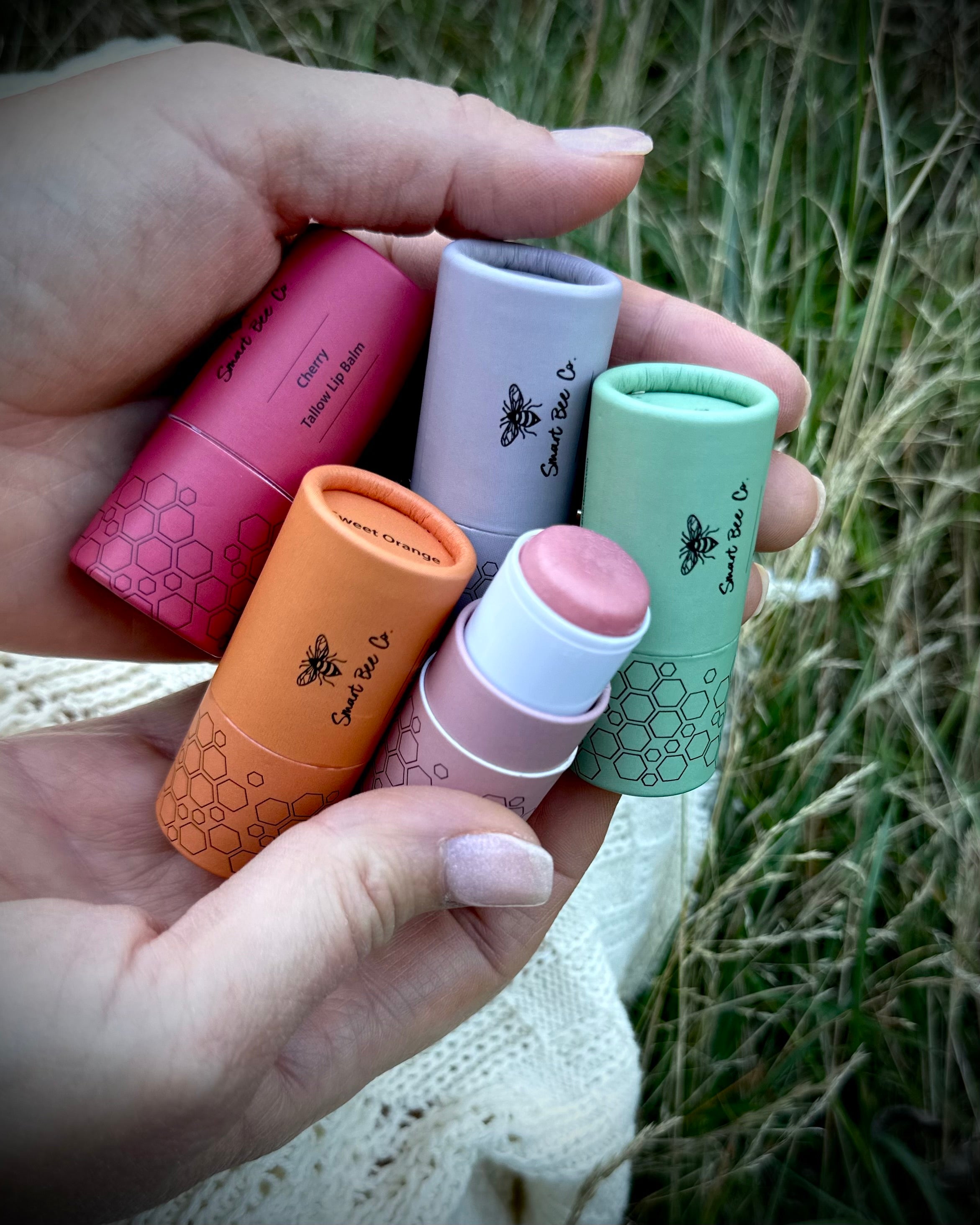 Hand holding five lip balms of different colors with visible branding.