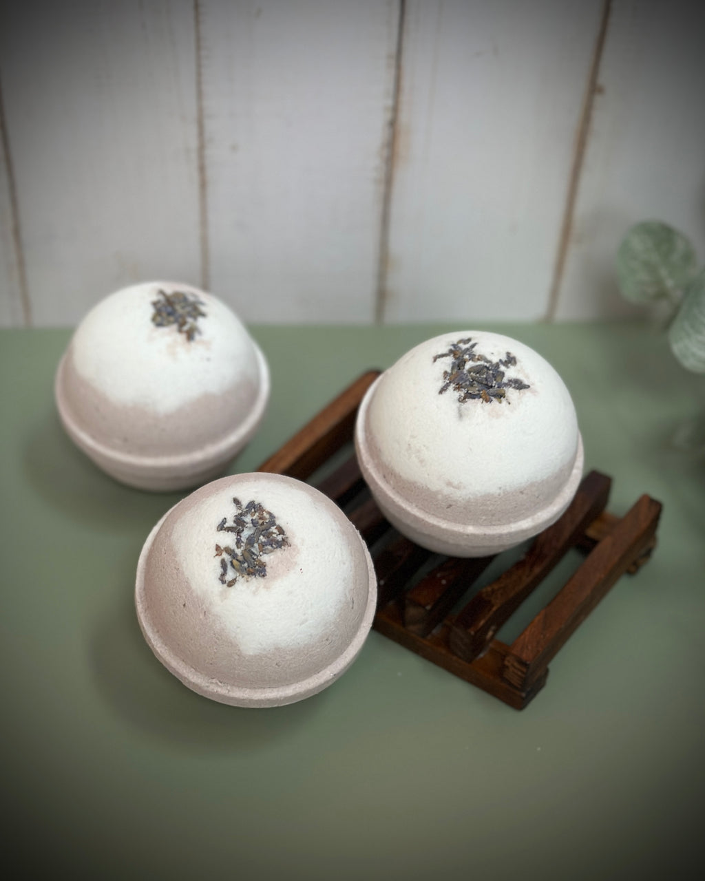 Three bath bombs with decorative elements on a wooden stand against a white wooden panel background.