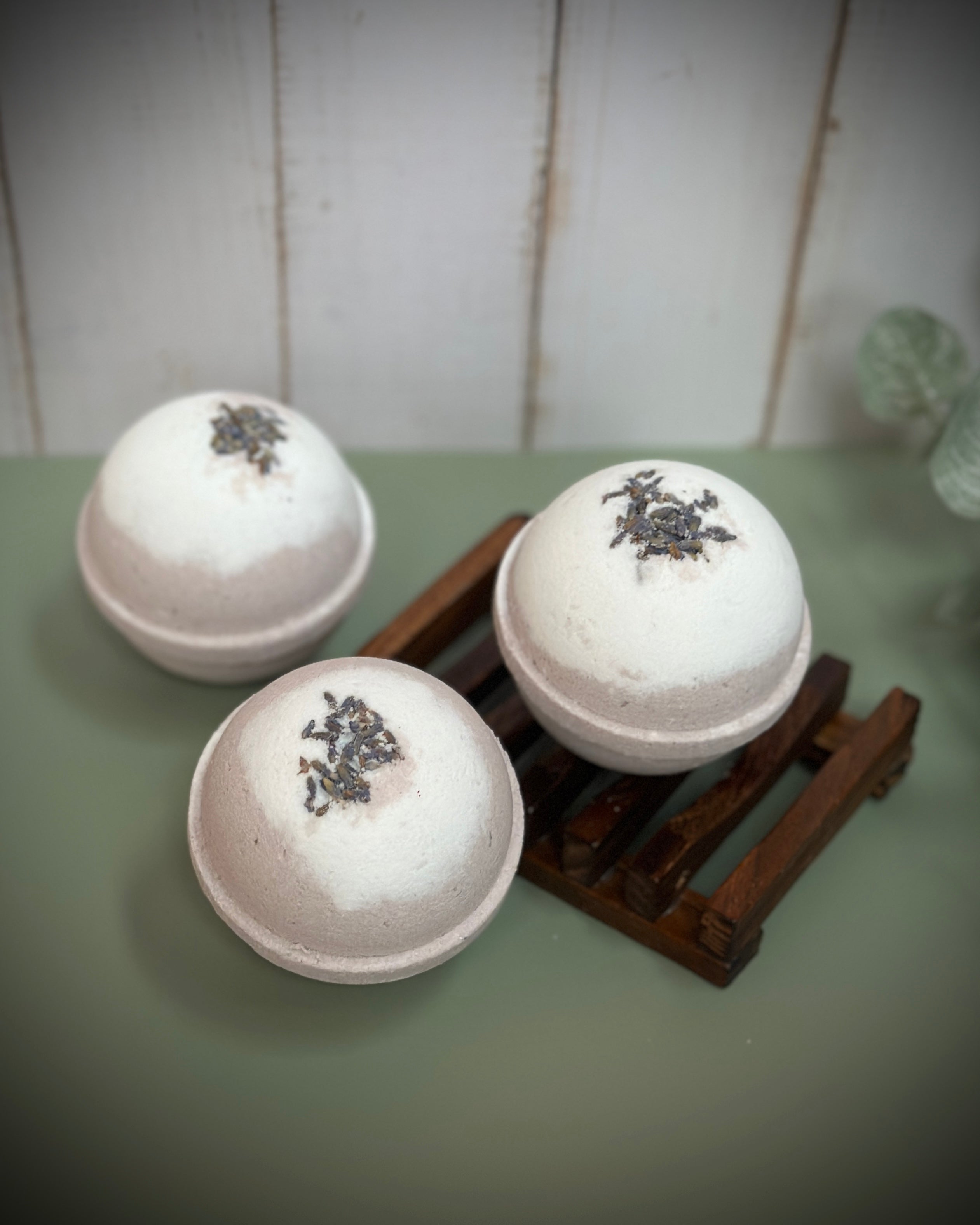 Three bath bombs with decorative elements on a wooden stand against a white wooden panel background.