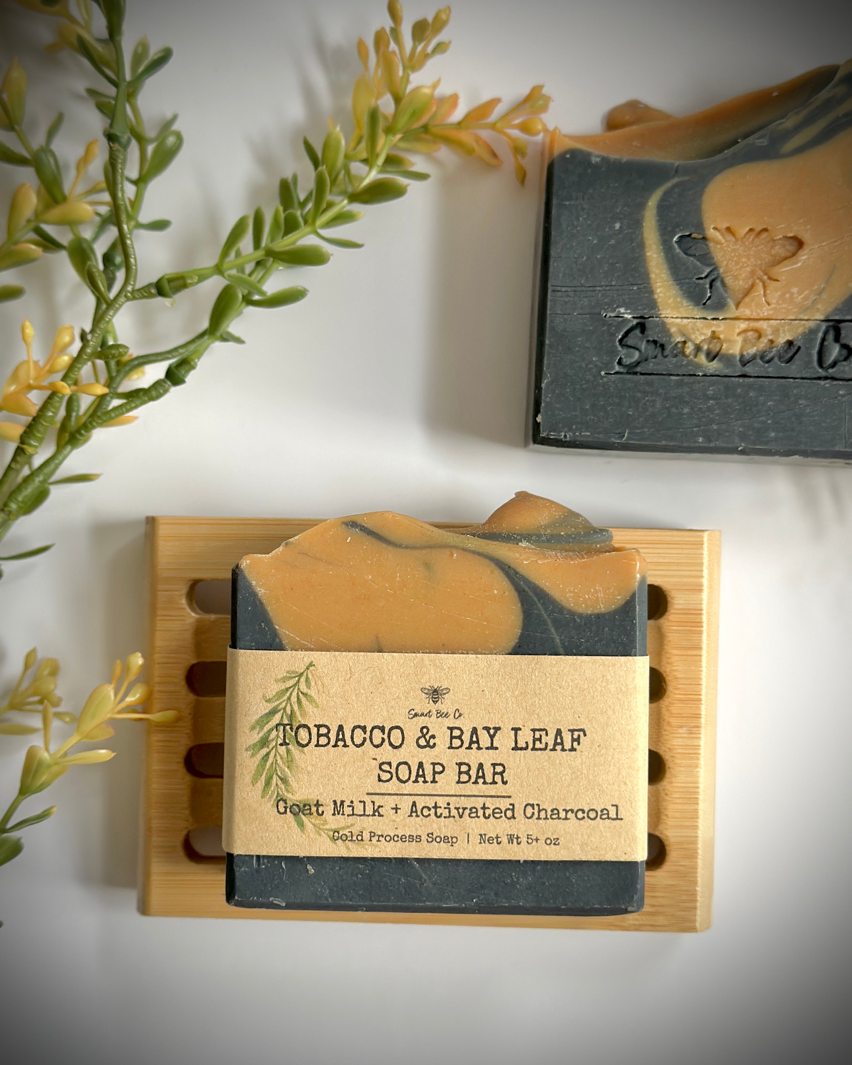Tobacco Bay Leaf soap bar on a wooden soap dish with a plant in the background