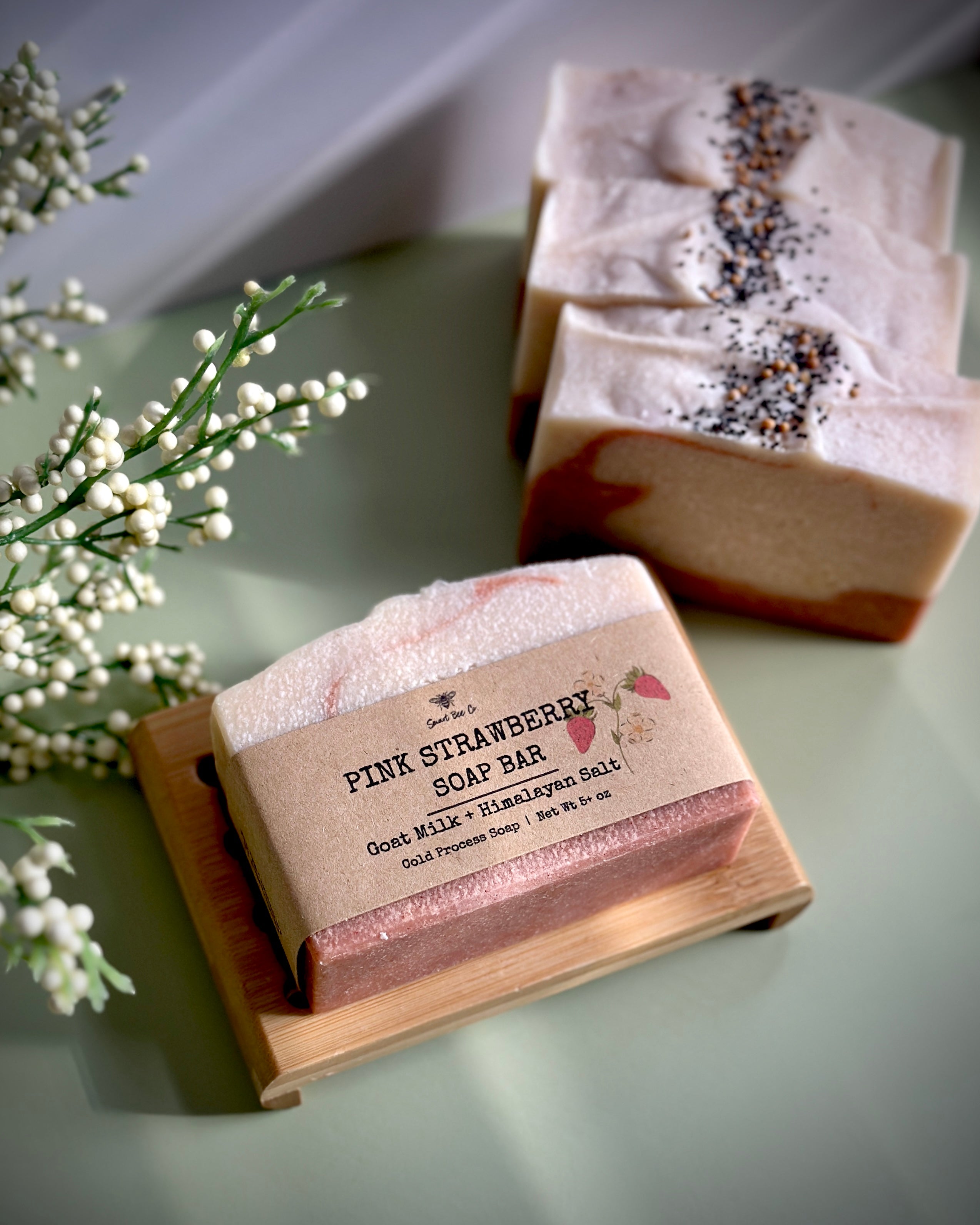Pink strawberry soap bar on a wooden stand with other soap bars in the background.