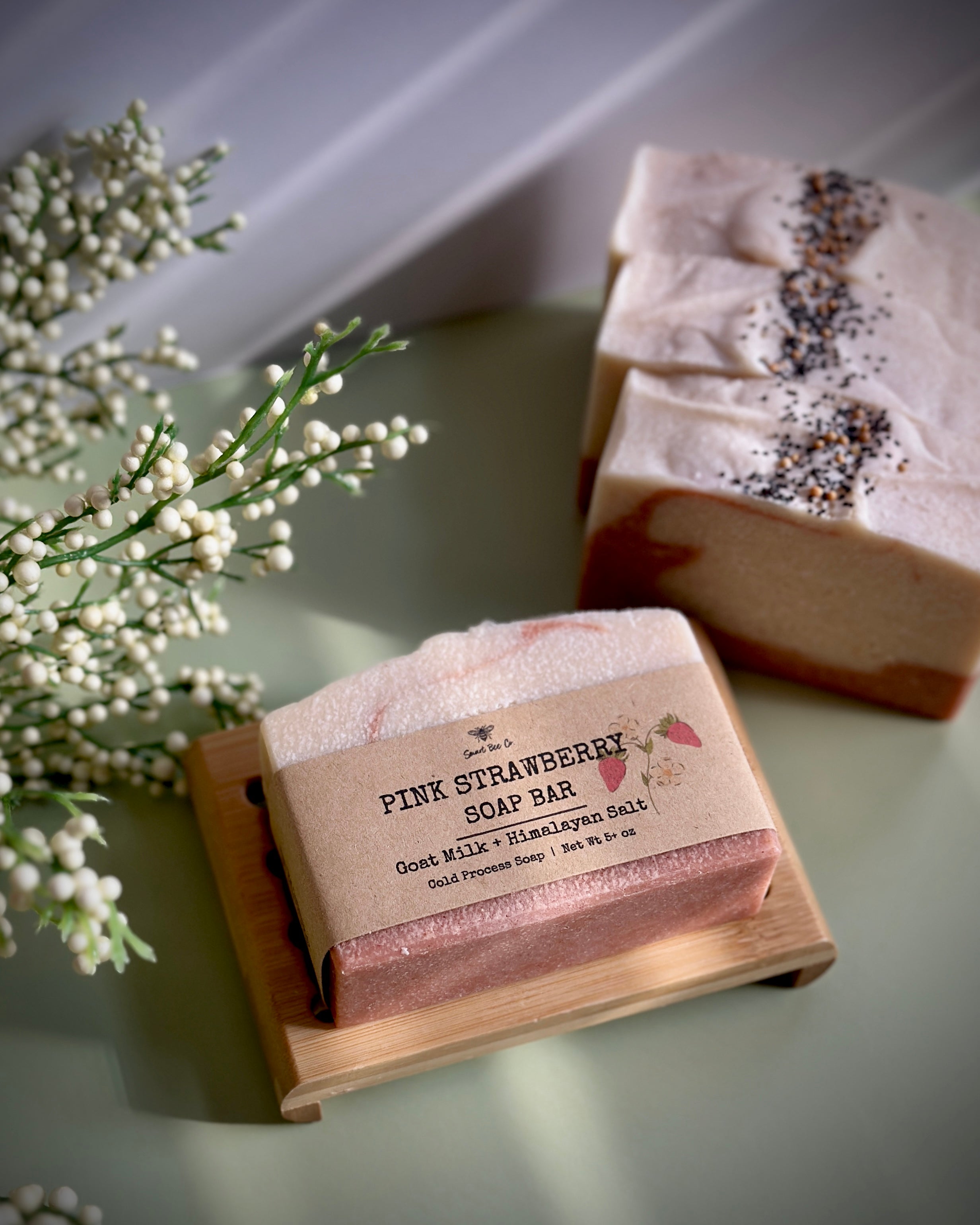 Pink strawberry soap bar on a wooden stand with a plant in the background