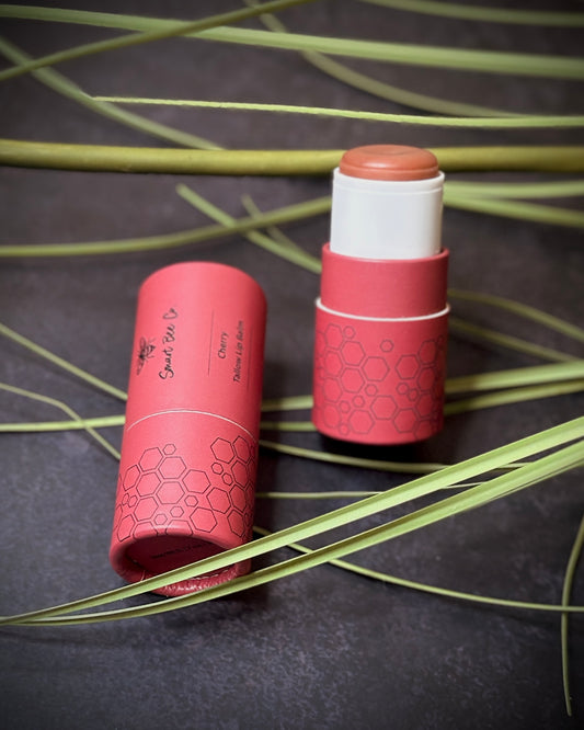 Two cherry flavor tallow lip balm sticks with hexagonal patterns on a dark surface with green leaves.