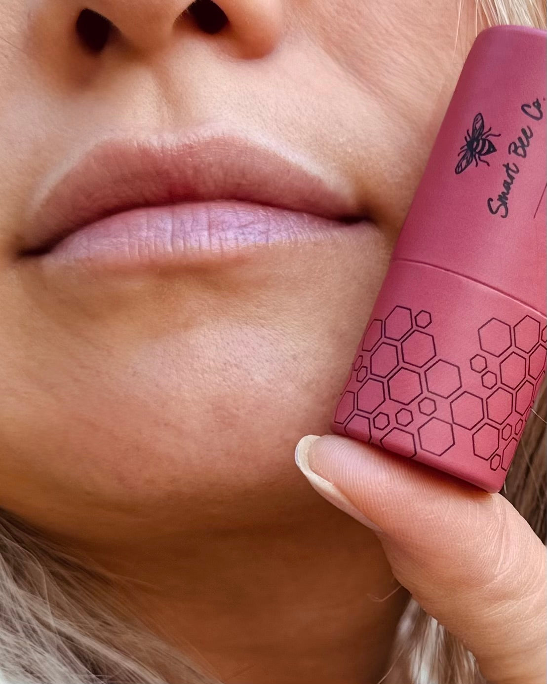 Close-up of a person holding a pink red cherry tallow lip balm with a hexagonal pattern.